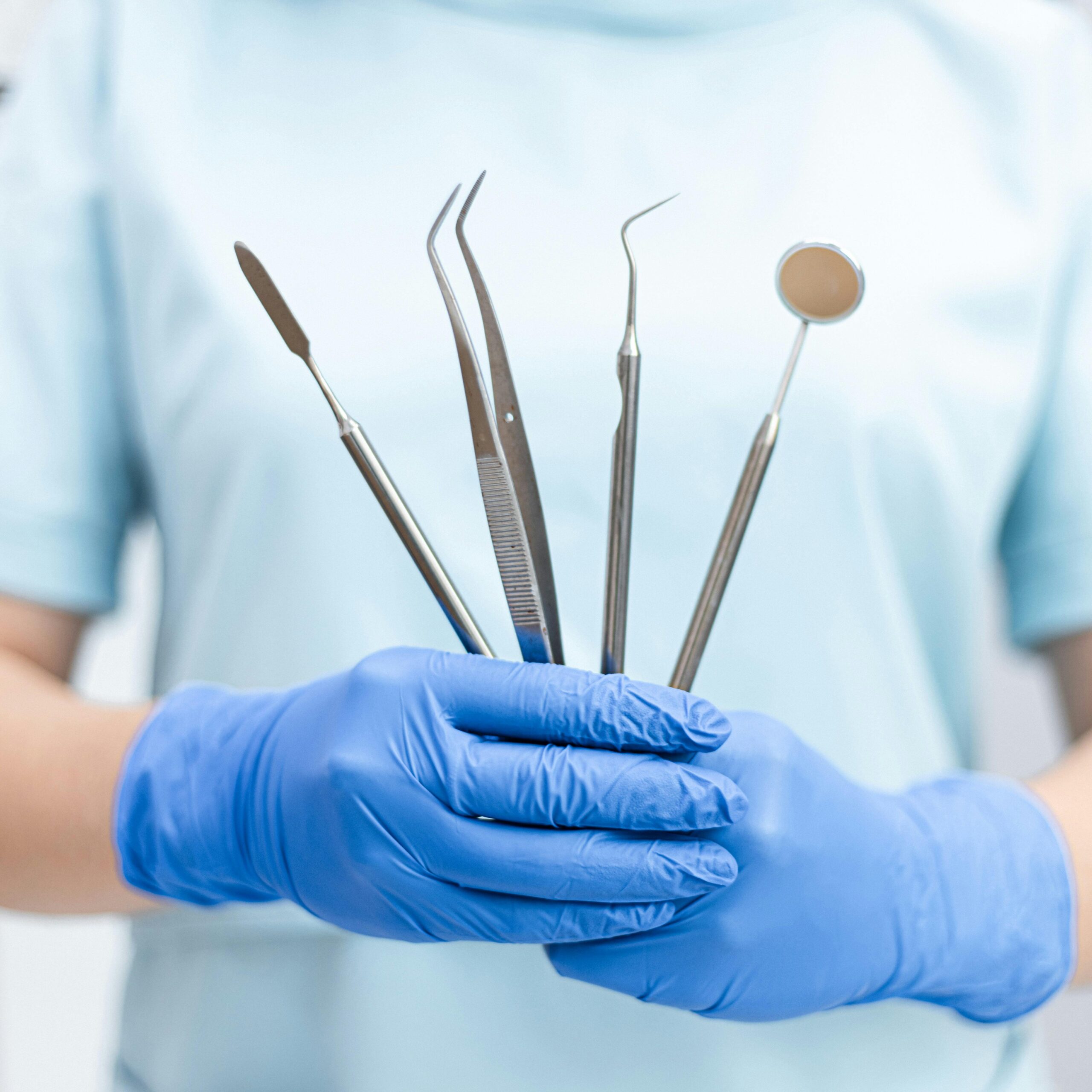 Procedures A dentist holding various dental tools in gloved hands, ready for use.